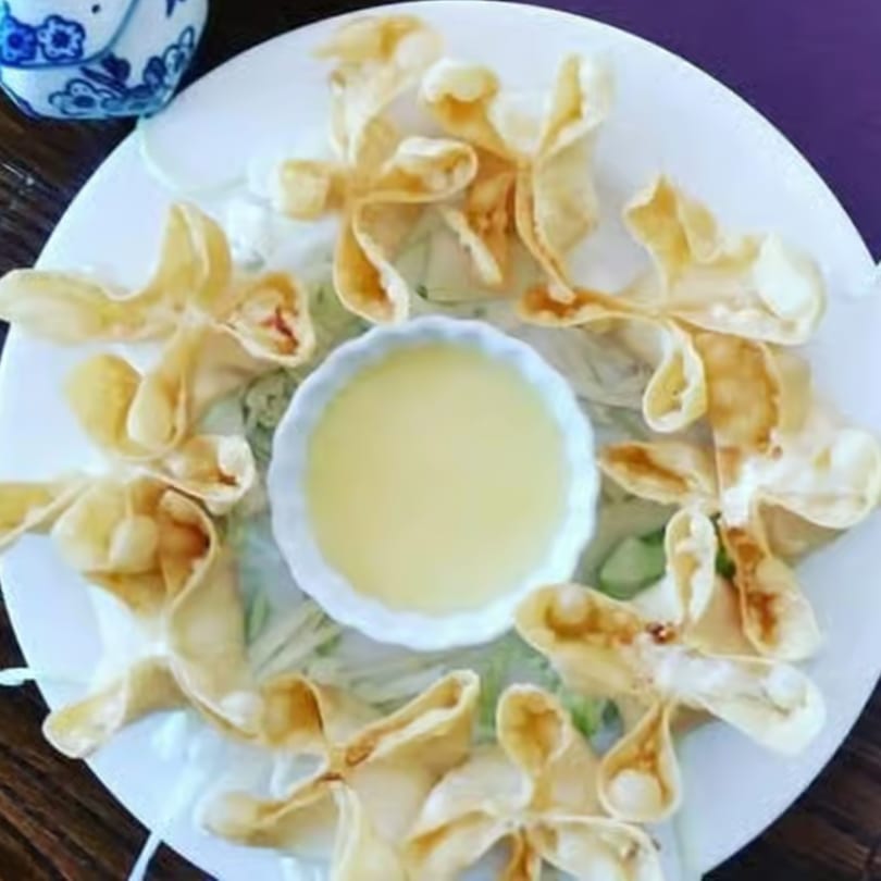 Crab rangoons arranged in a circle around a small bowl of dipping sauce on a white plate.