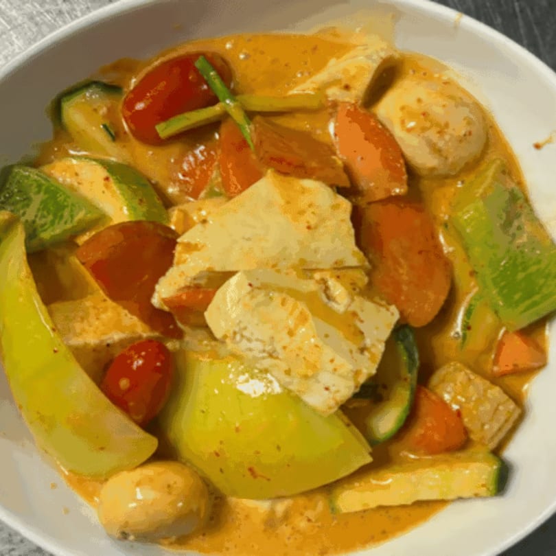 A bowl of Chinese curry with tofu, zucchini, tomatoes, and mushrooms in a rich sauce.