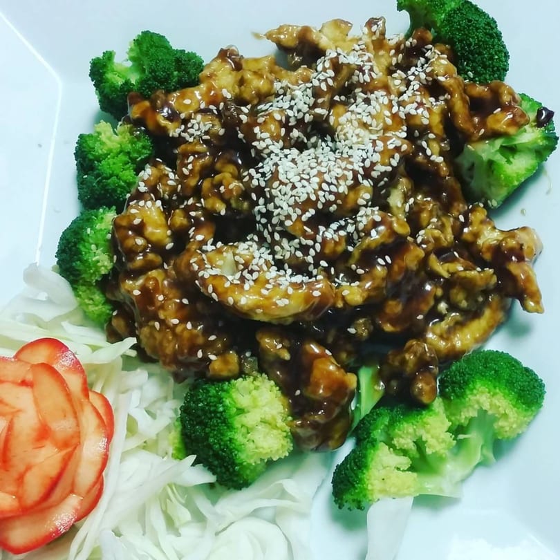 China 10's sesame chicken with broccoli florets, shredded cabbage, and a strawberry garnish.