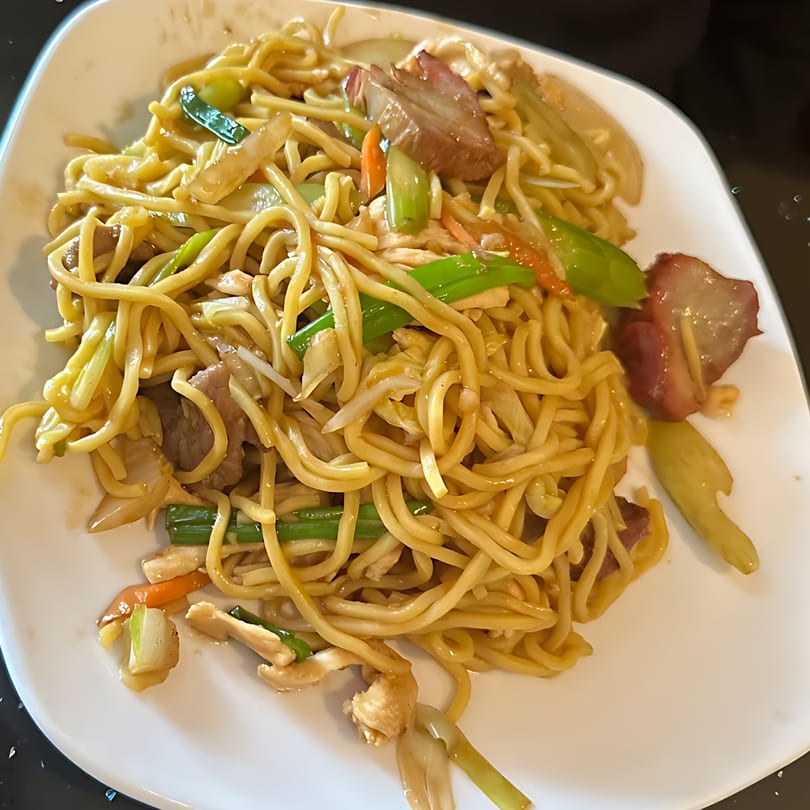 China 10's delicious lo mein noodles with vegetables and sliced pork on a white plate.